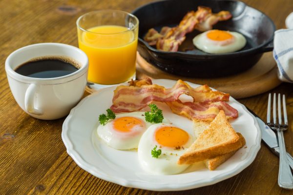 American breakfast with sunny side up eggs, bacon, toast, pancakes, coffee and juice, wood background
